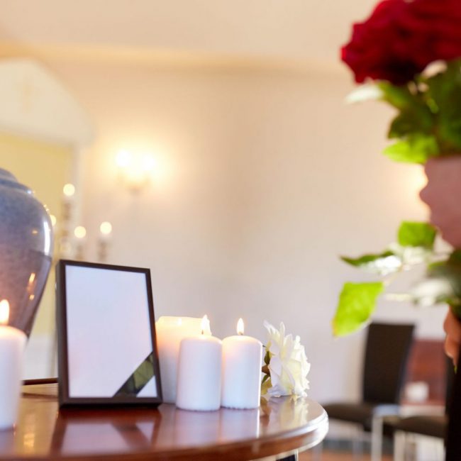 cremation, people and mourning concept -  cinerary urn, photo frame with black ribbon and woman holding red roses at funeral in church